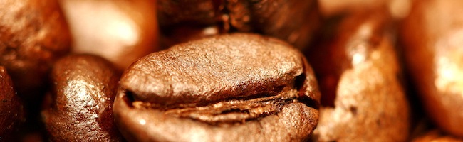 Tasse de café fumant avec une cuillère et des grains de café sur un fond sombre